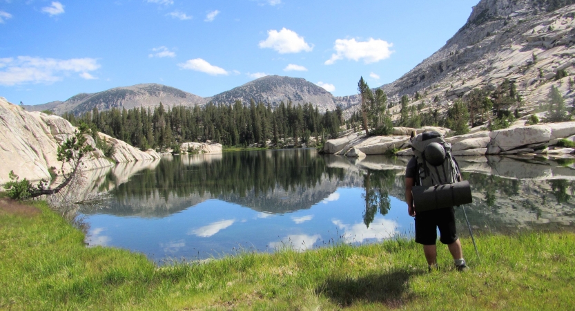 a student stands beside a blue alpine lake reflecting a mountainous landscape